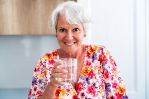 Beautiful senior old woman with gray hair drinking glass of water at home - Youthful elderly granmother spending quality time at home